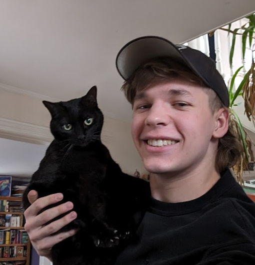 A selfie of keeper wearing a baseball cap and holding a freightened black cat on his shoulder